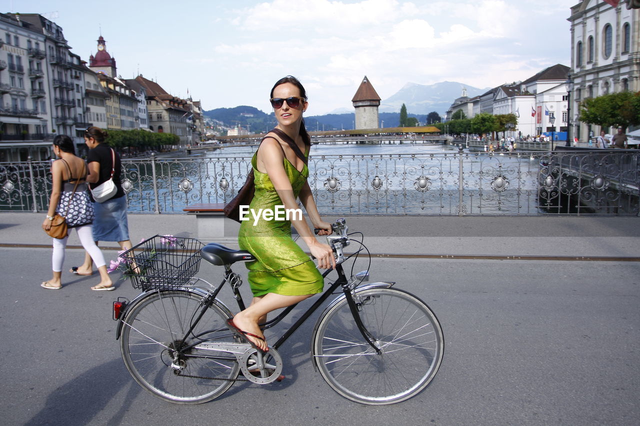 FULL LENGTH OF YOUNG WOMAN RIDING BICYCLE ON CITY STREET