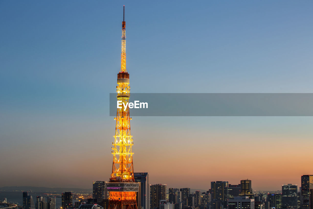 Illuminated tokyo tower amidst city against clear sky during sunset