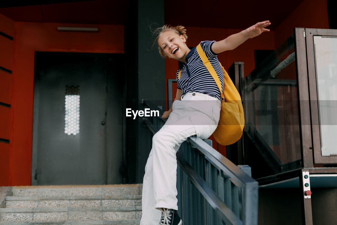 A teenage girl laughs and slides down the railing on her way to school. a cheerful girl hurries 