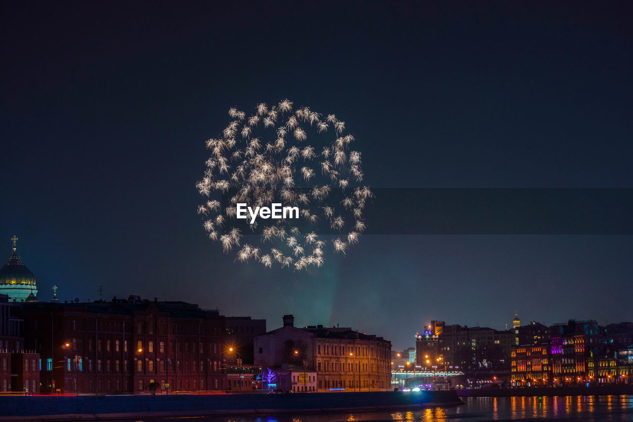 Firework display over city against clear sky at night