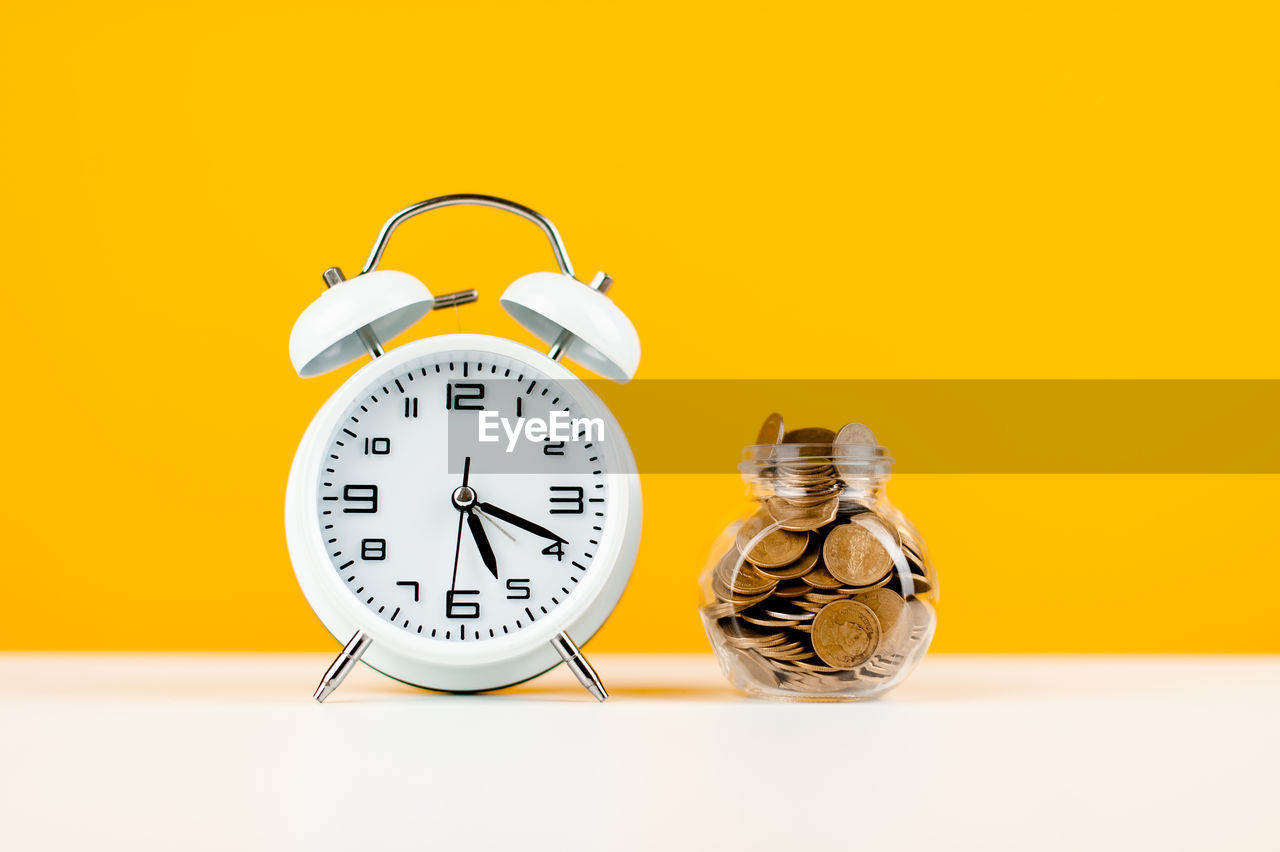 close-up of alarm clock with model home against yellow background