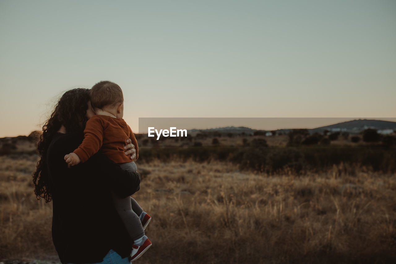 Rear view of mother and son on field against sky