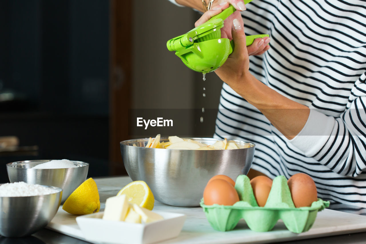 Woman squeezing fresh lemon juice while cooking apple pie in the modern kitchen