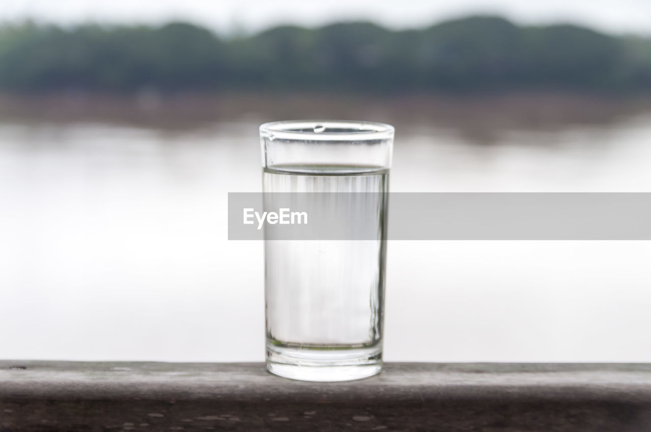 Glass of drinking water on railing against river