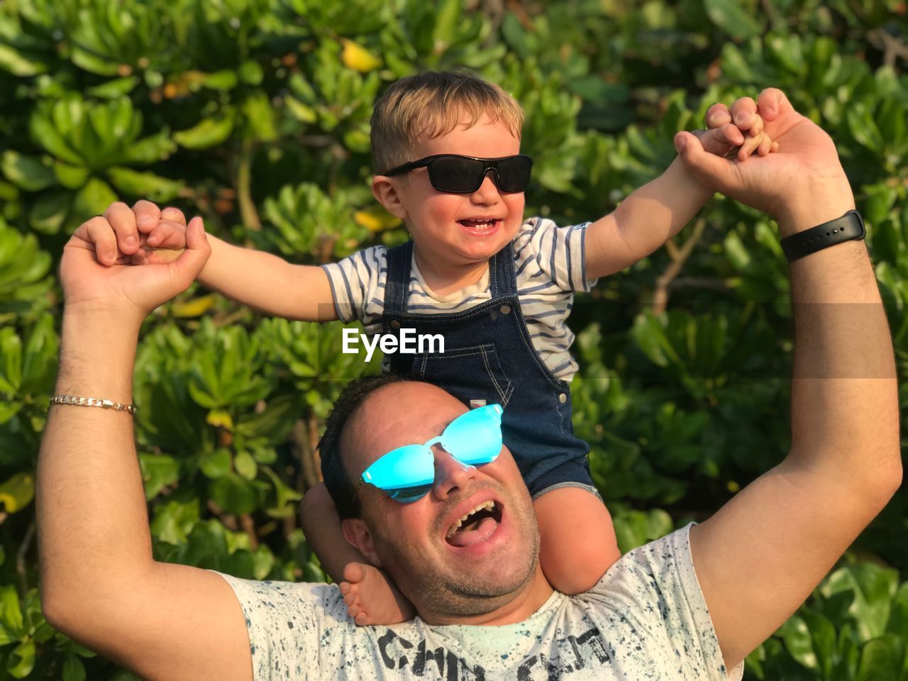 Cheerful father carrying son on shoulders against trees