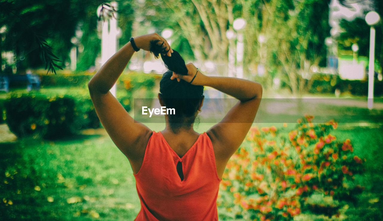 Rear view of young woman tying hair while standing against trees in park