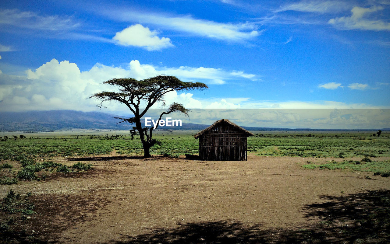 BUILT STRUCTURE ON FIELD BY HOUSE AGAINST SKY