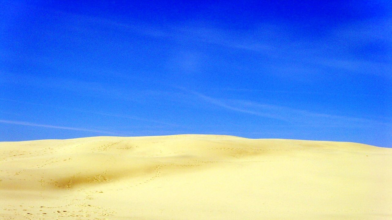 Low angle view of sand dune against blue sky