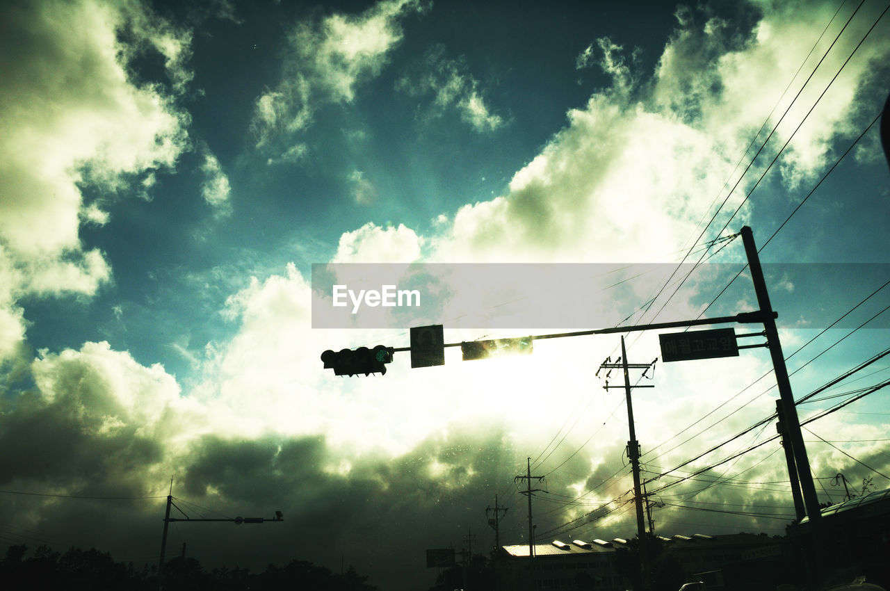 Low angle view of silhouette traffic stop light amidst electricity pylons against sky