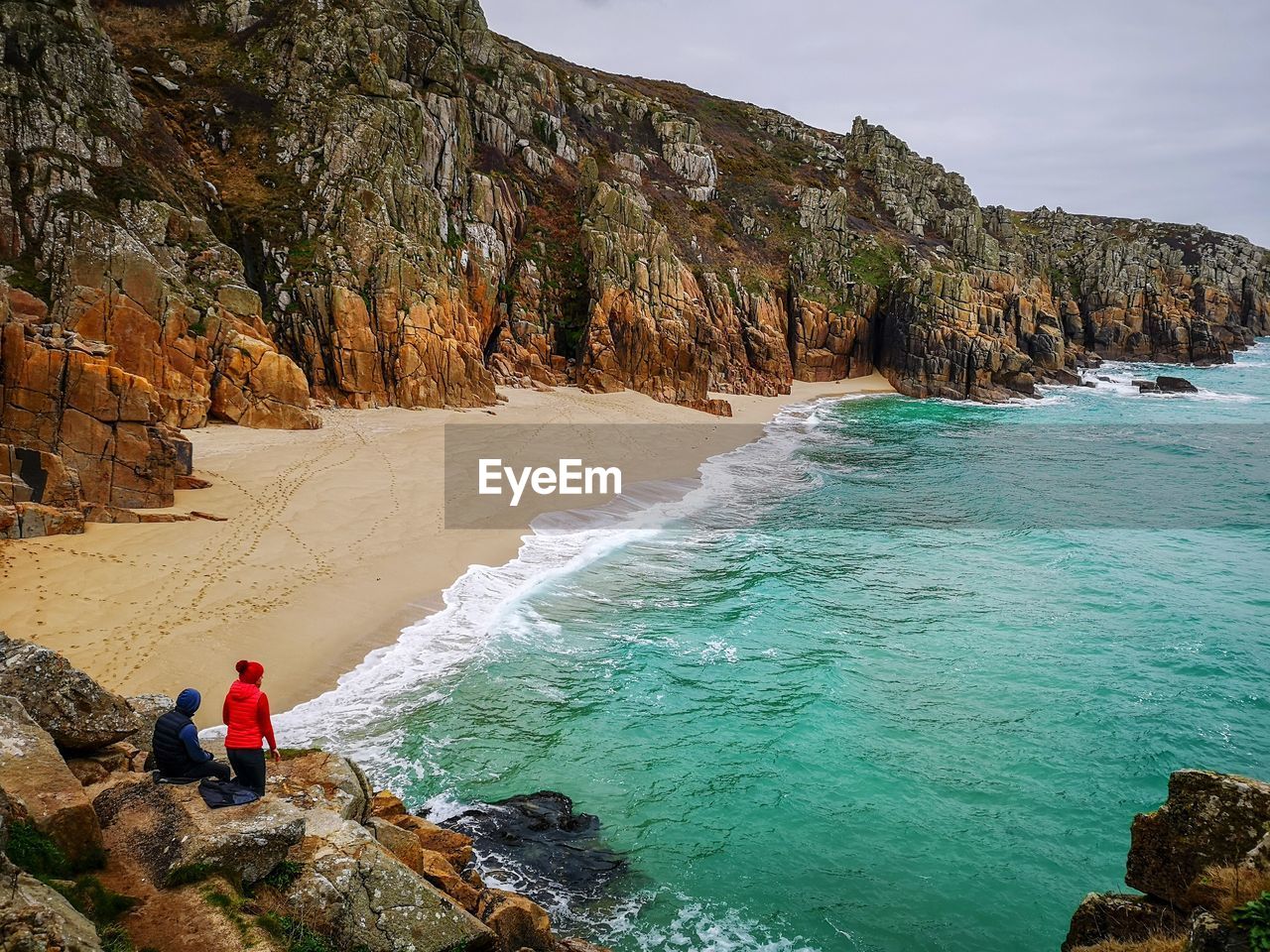 REAR VIEW OF PERSON ON ROCKS BY SEA AGAINST ROCK FORMATION