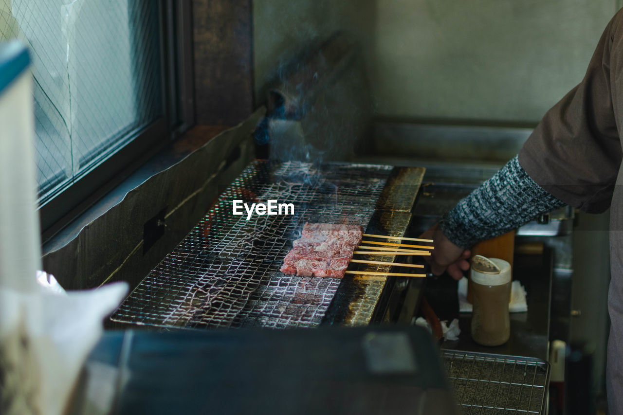 Midsection of person preparing meat on barbecue grill