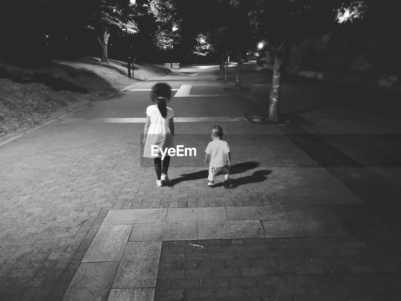 Rear view of girl walking with brother on footpath at night