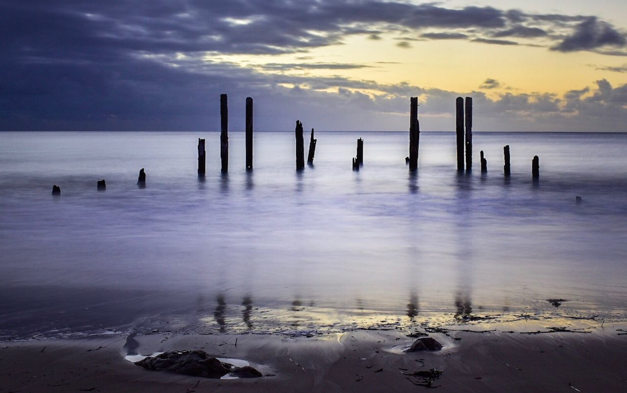 Wooden posts at shore during sunset