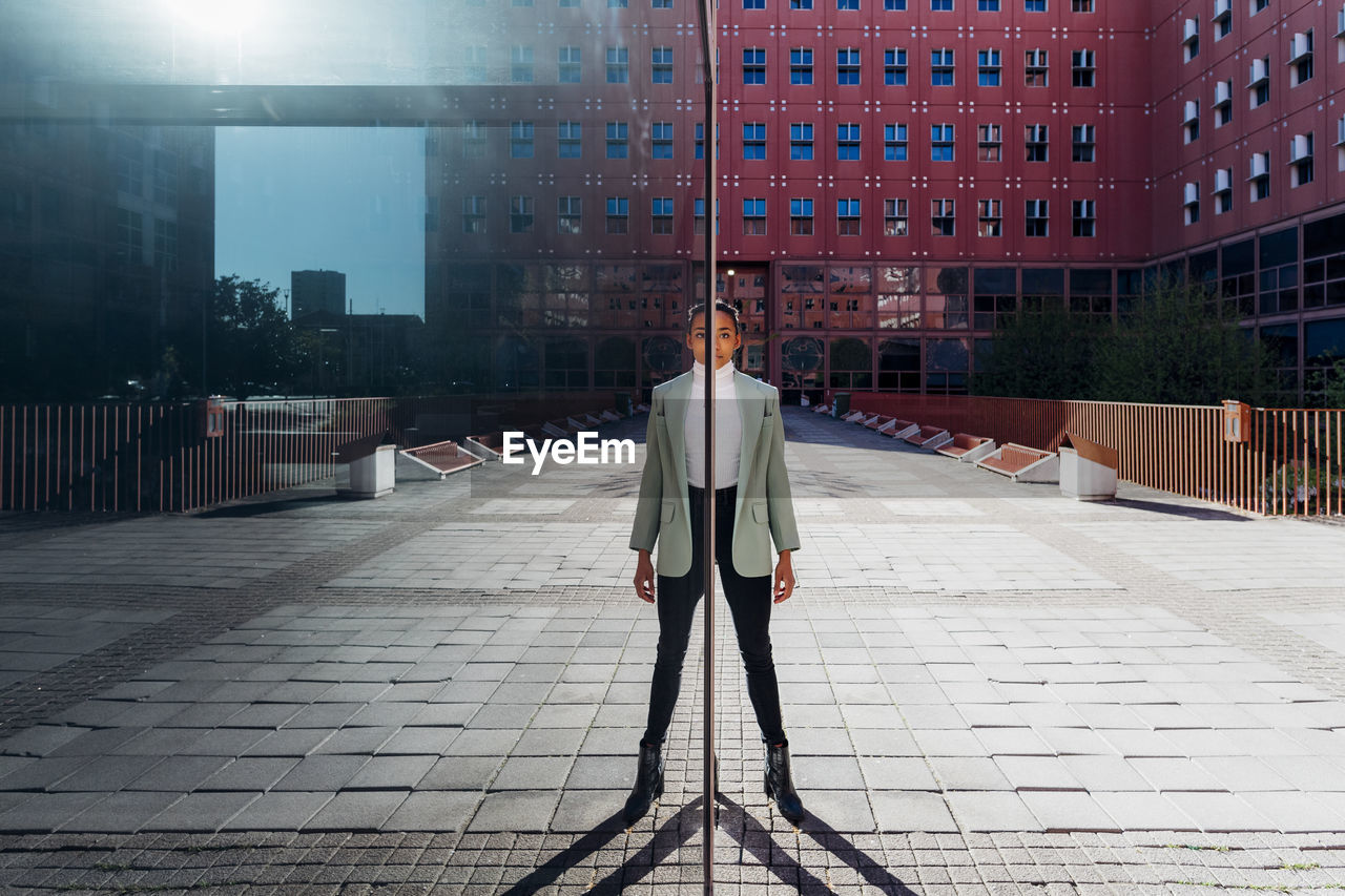 Reflection of young businesswoman on glass wall in financial district