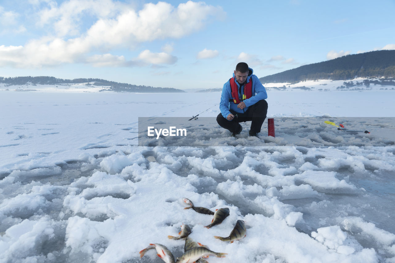 Fisherman fishing on snow covered lake against sky