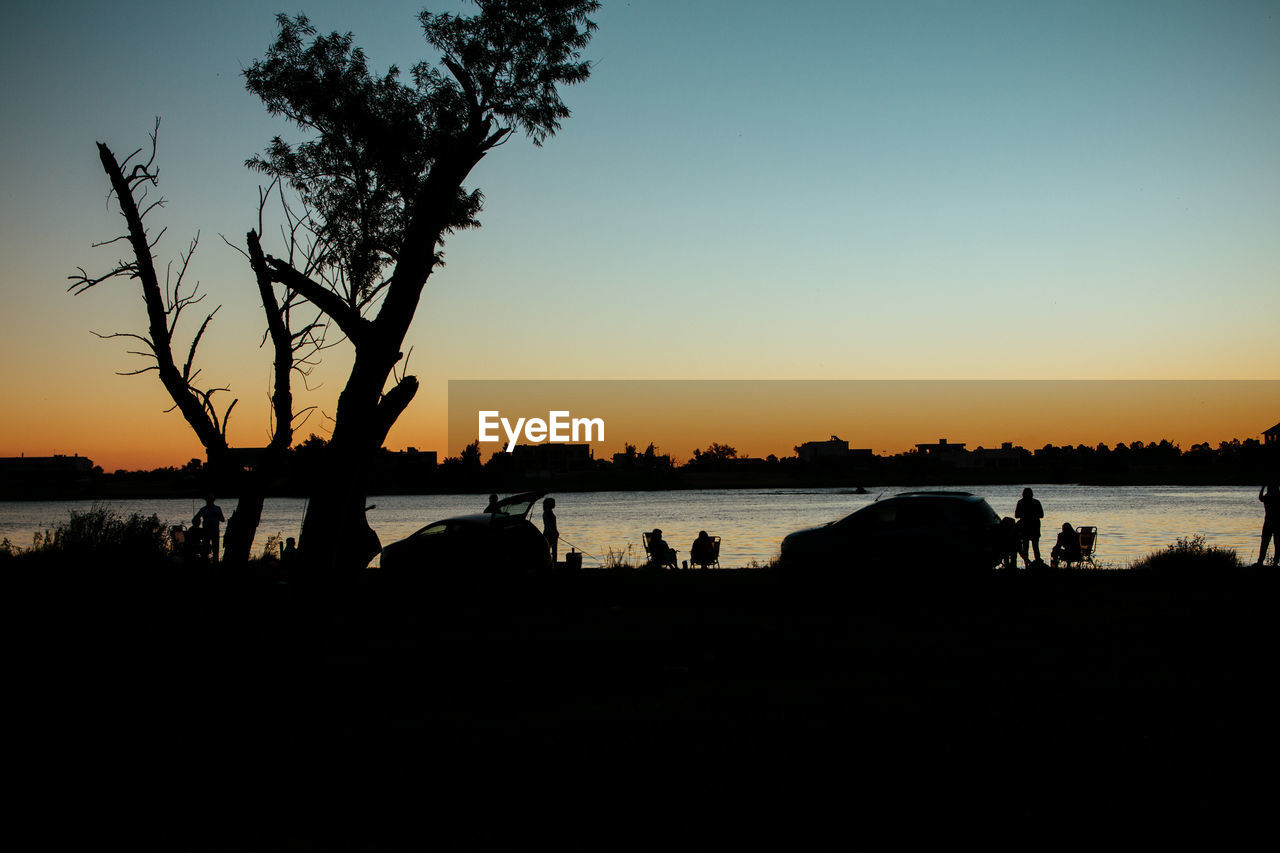 SILHOUETTE PEOPLE BY LAKE AGAINST CLEAR SKY AT SUNSET