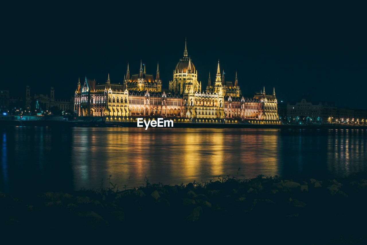 Illuminated hungarian parliament building by river against clear sky at night