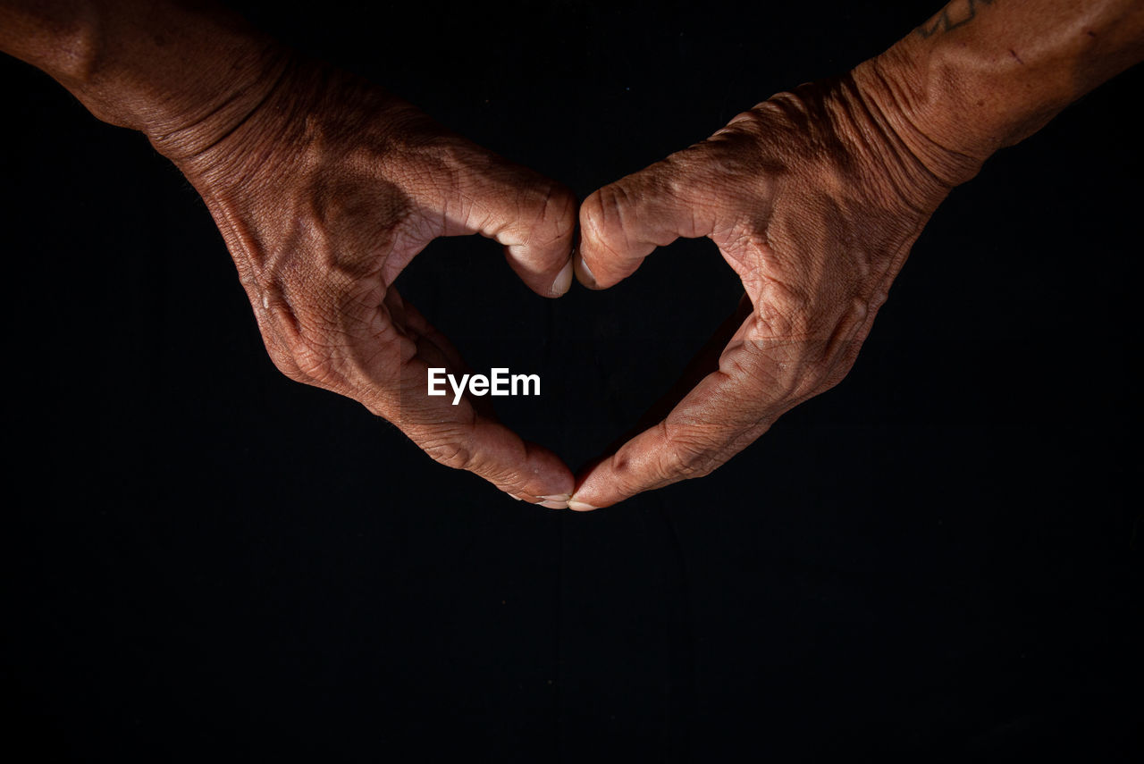 hand, black background, arm, finger, emotion, studio shot, darkness, heart shape, positive emotion, adult, close-up, indoors, love, limb, men, one person