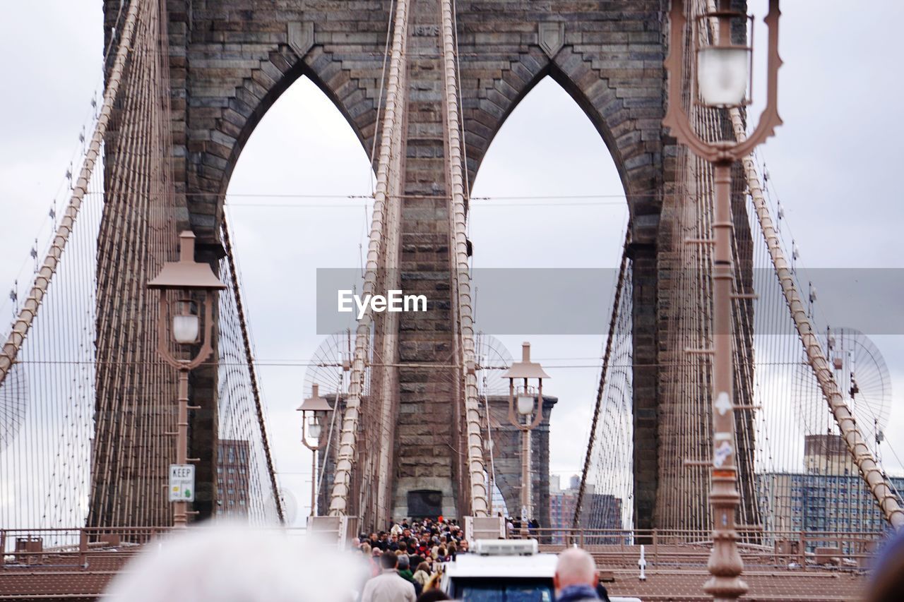 People on brooklyn bridge against cloudy sky