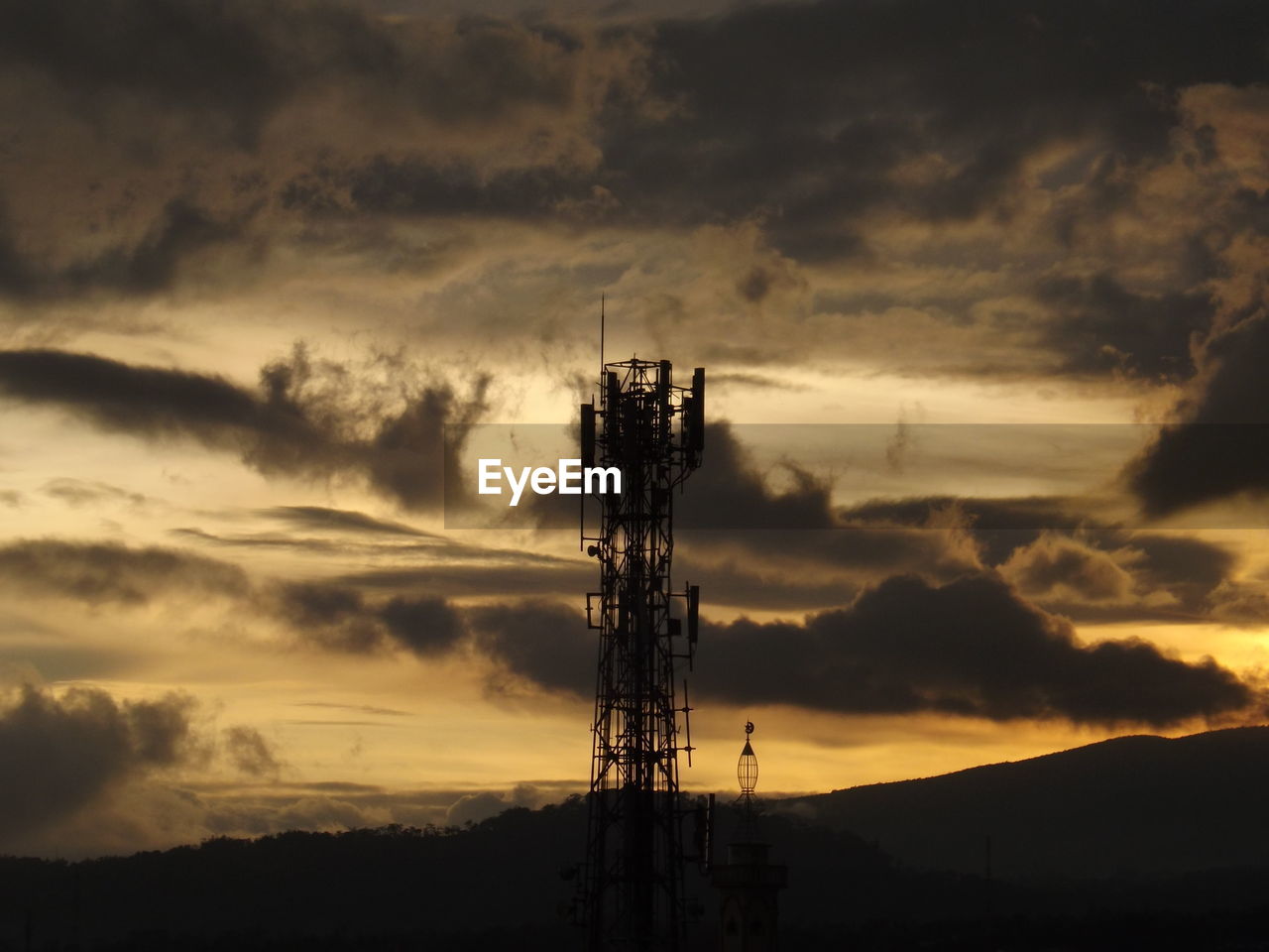 SILHOUETTE OF COMMUNICATIONS TOWER AGAINST CLOUDY SKY