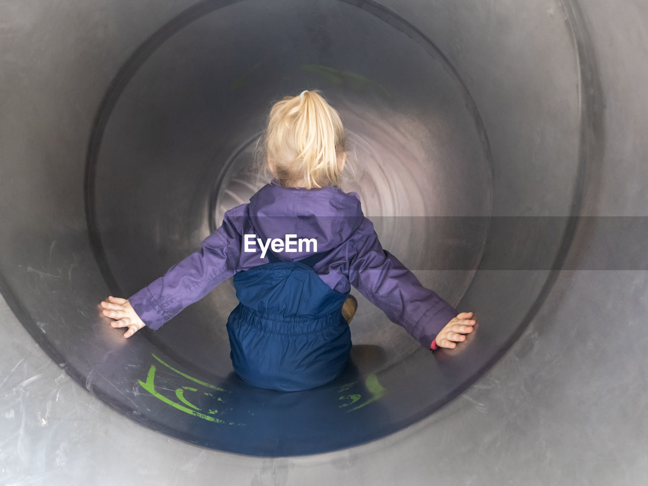 Blond girl with arms outstretched playing in tube slide at playground