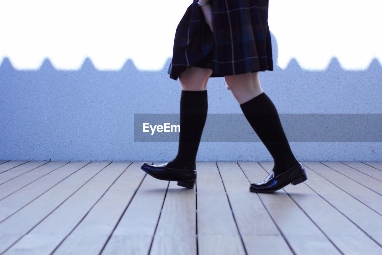 Low section of schoolgirl walking on footpath against wall