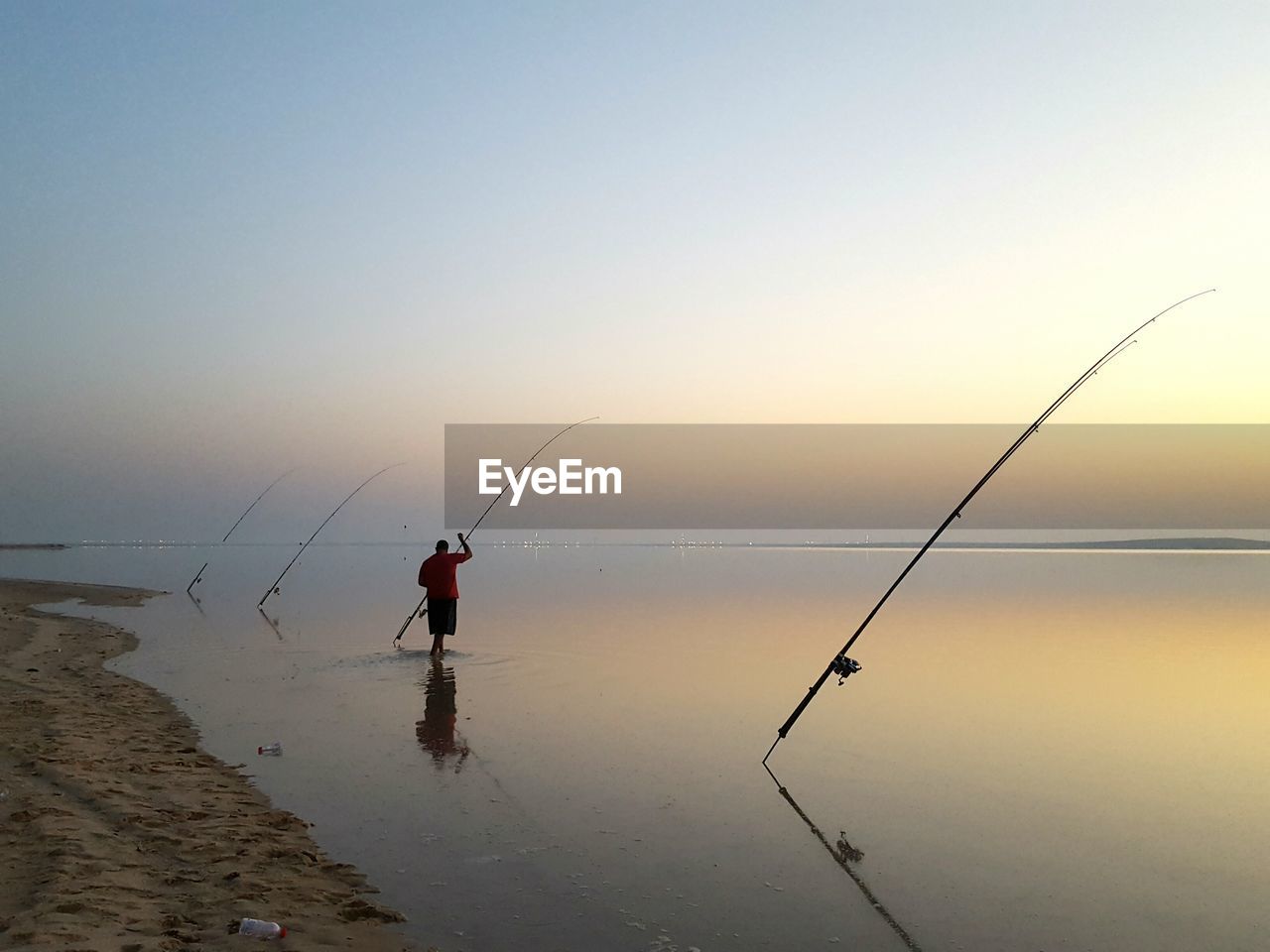 Rear view of man fishing in sea against clear sky during sunset