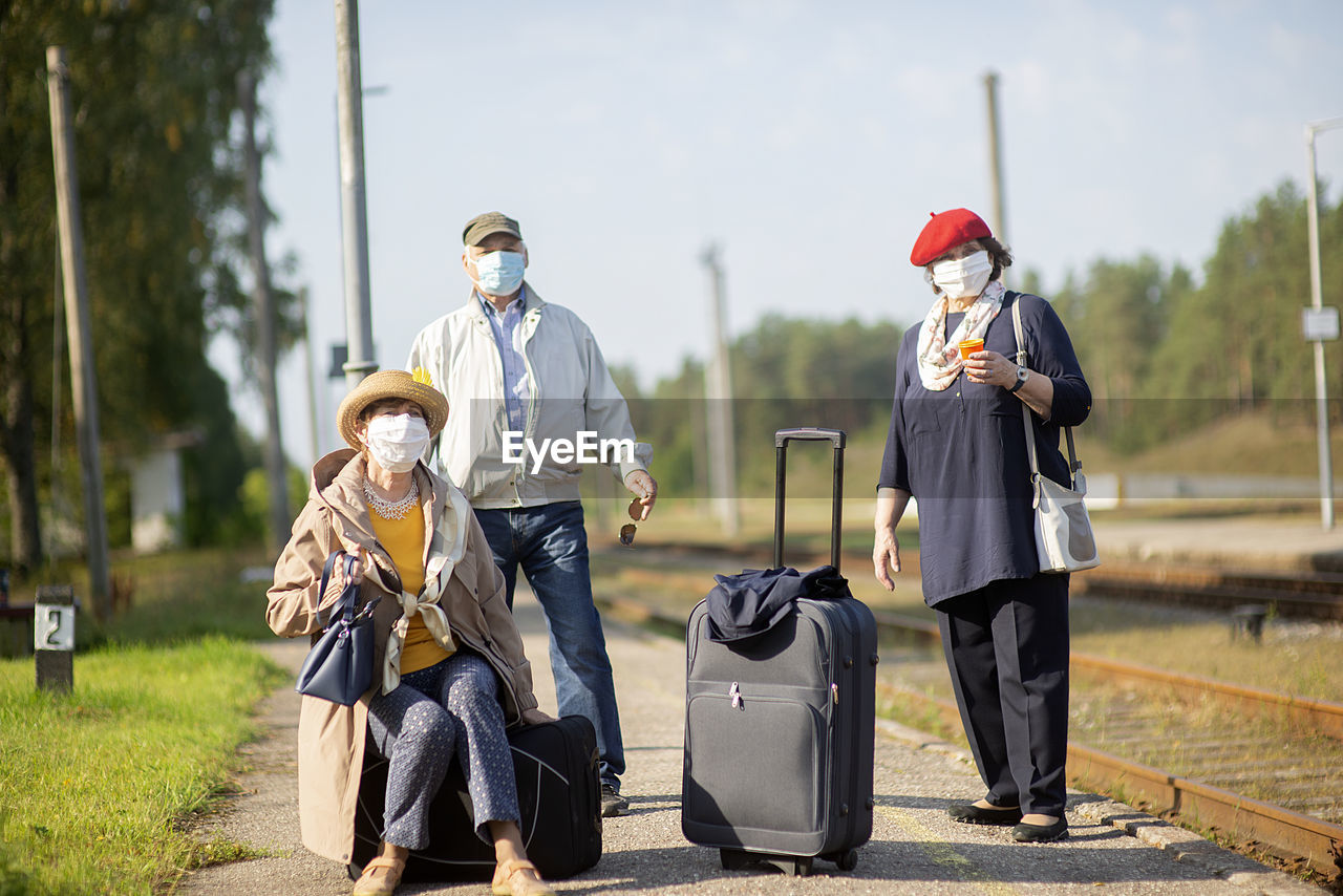 Positive elderly seniors people with face masks waiting train before traveling during a pandemic