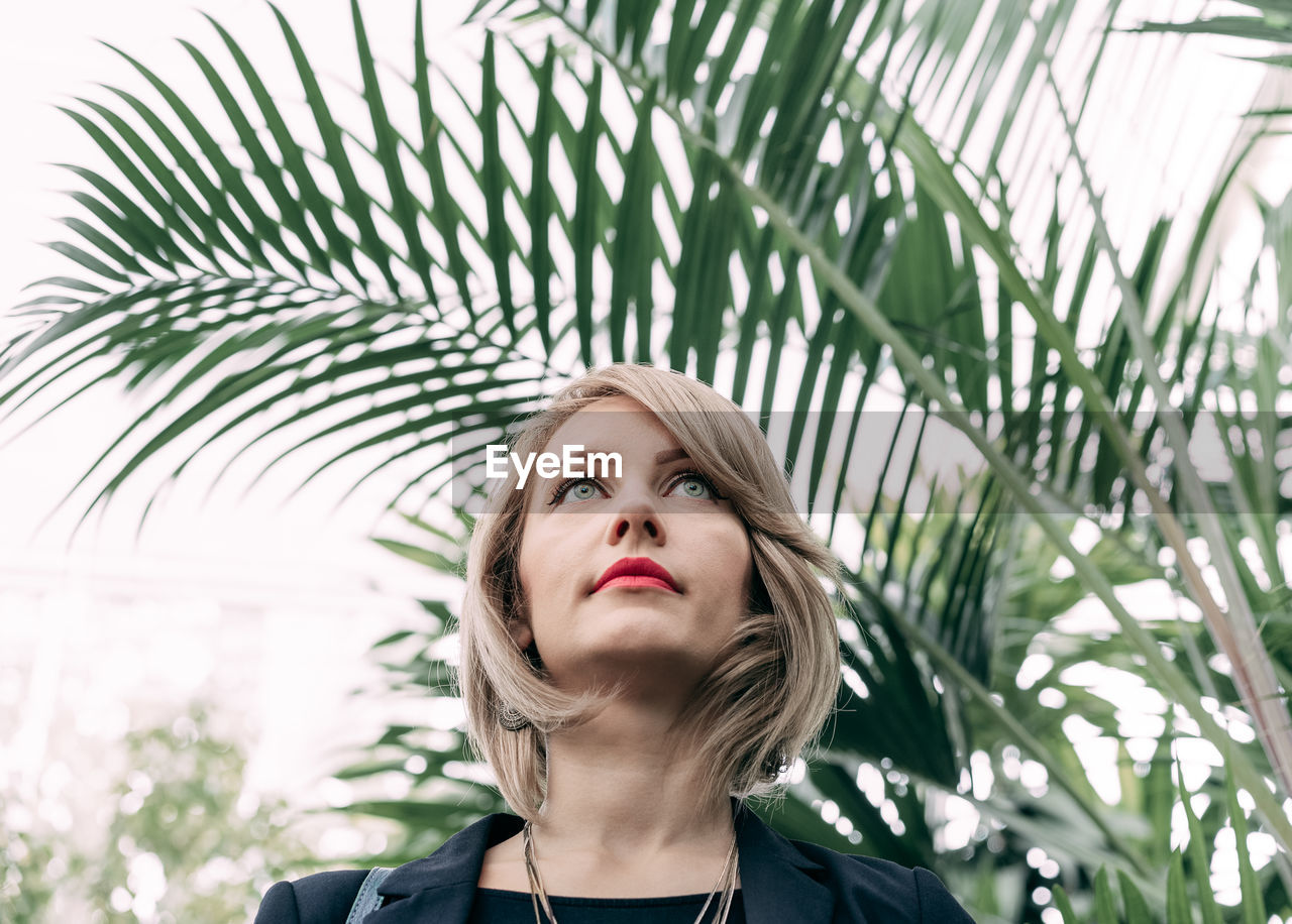 Low angle view of confident young woman looking away while standing against plants