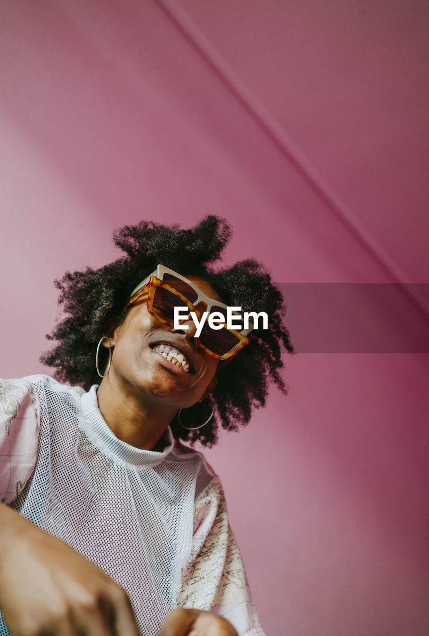 Smiling hipster woman wearing sunglasses against pink wall at home