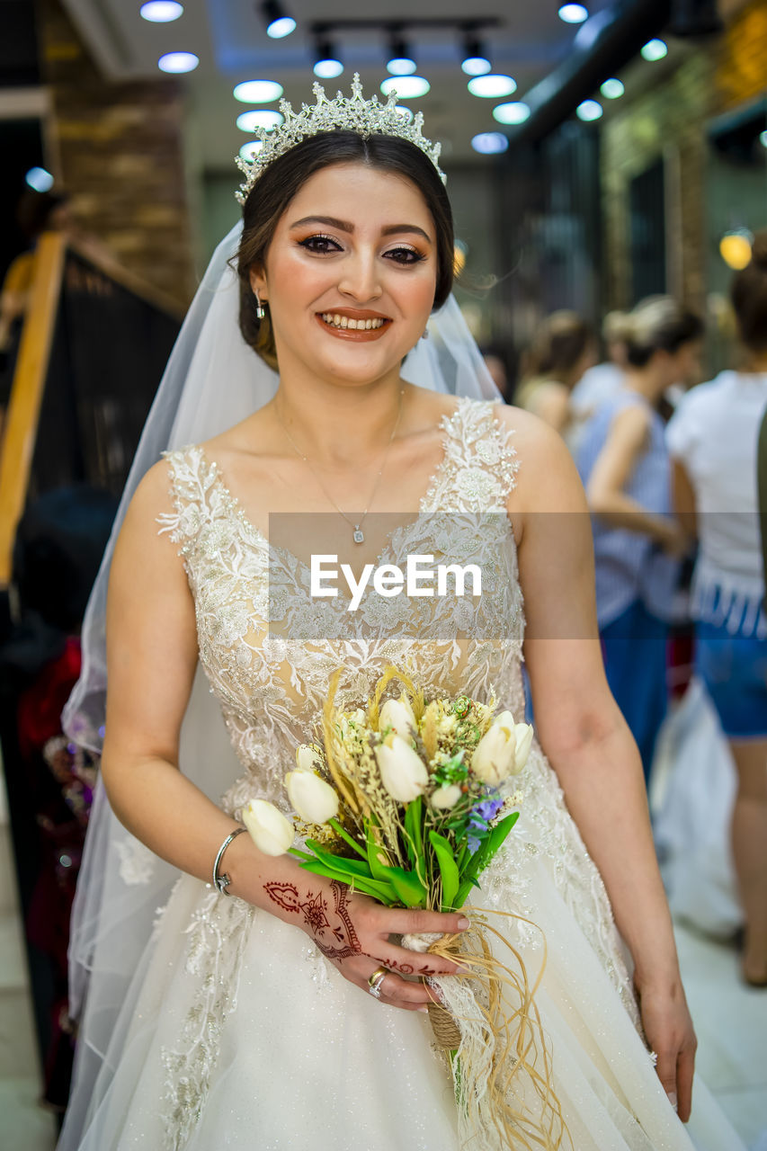 PORTRAIT OF SMILING WOMAN STANDING BY FLOWER BOUQUET