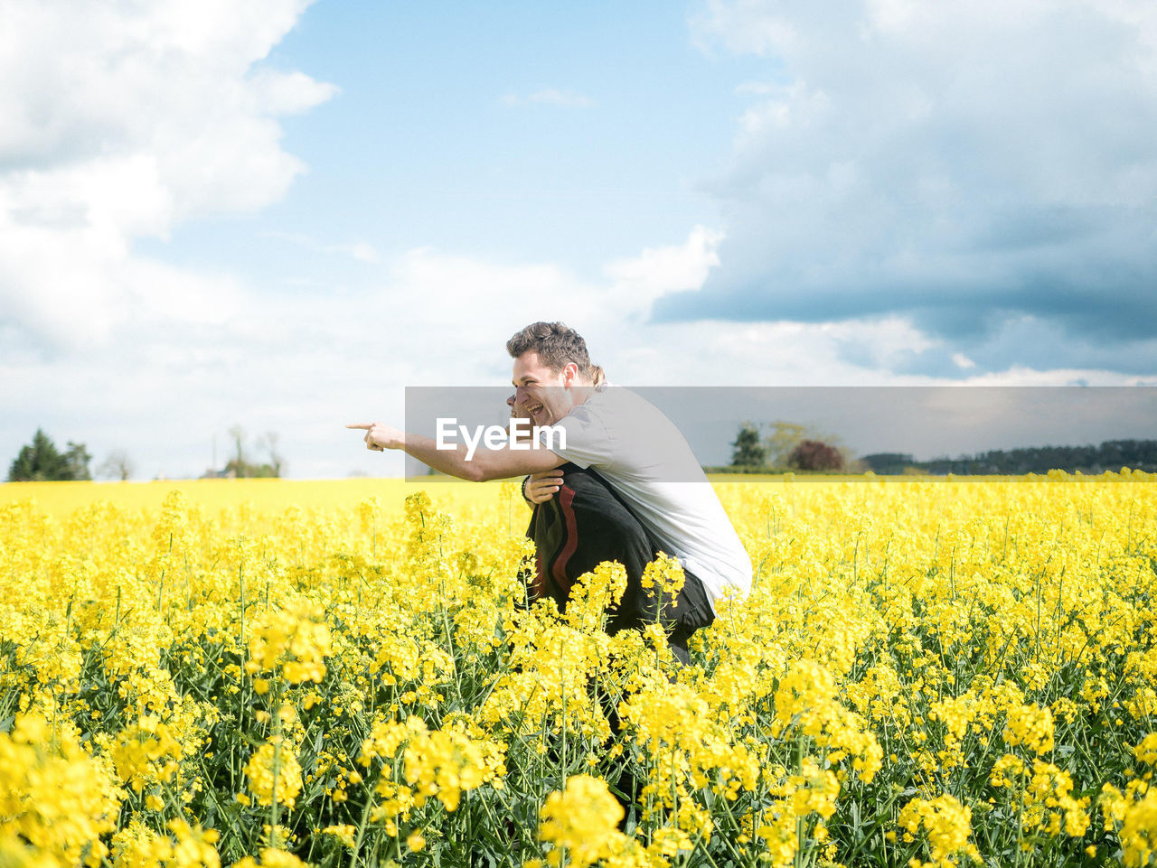 Woman piggybacking friend while standing on oilseed rape field