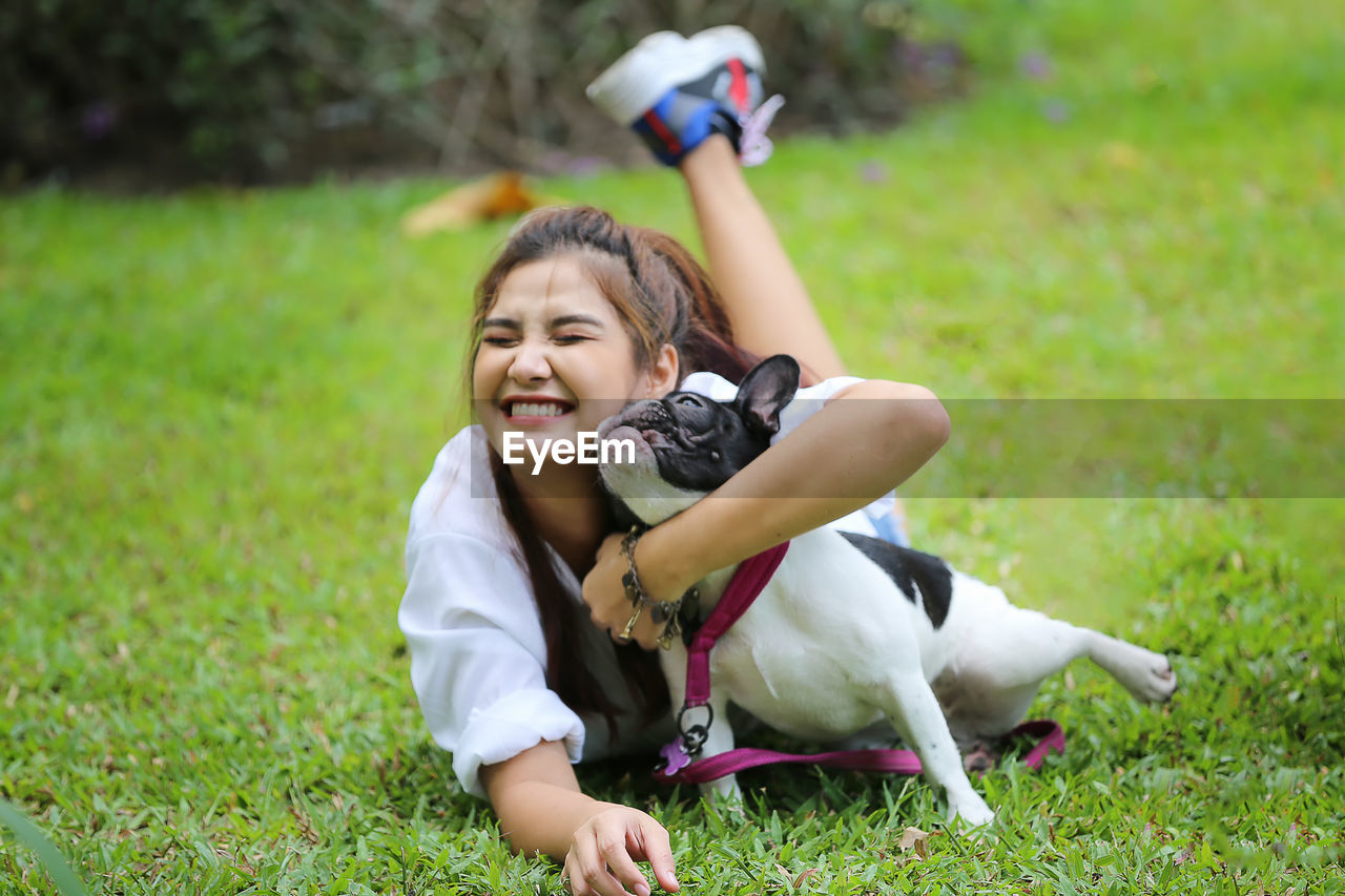 Full length of girl embracing dog while lying on grass