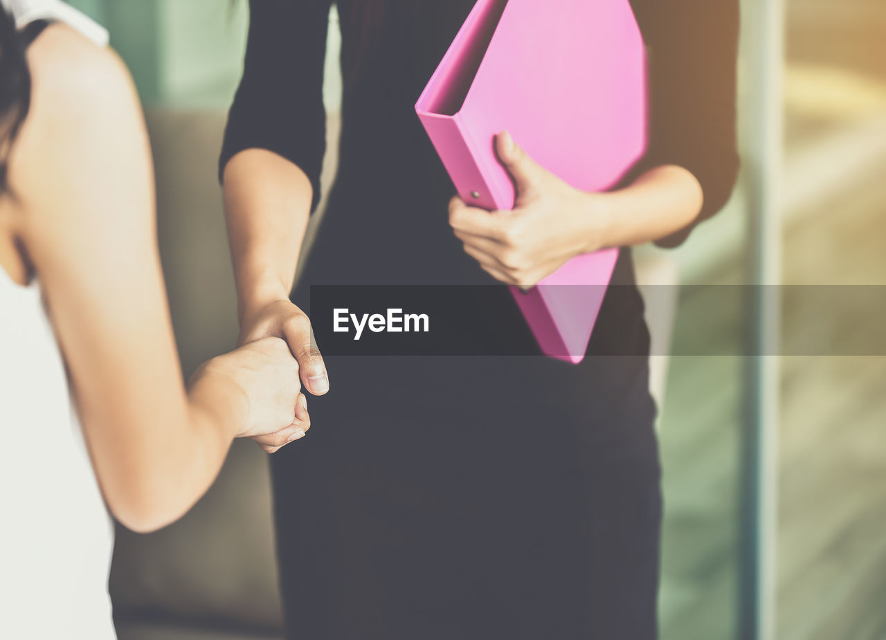 Midsection of female colleagues giving handshake while standing in office