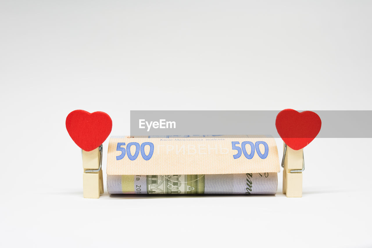 Close-up of red heart shaped clothespin with paper currency on white background