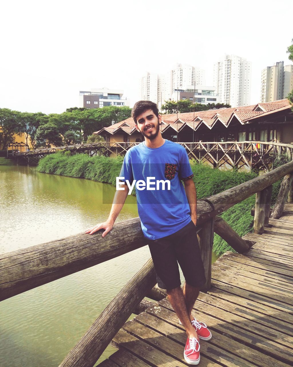 Smiling young man standing on wooden footbridge over canal