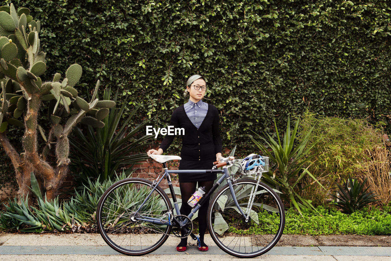 Portrait of businesswoman standing with bicycle against plants