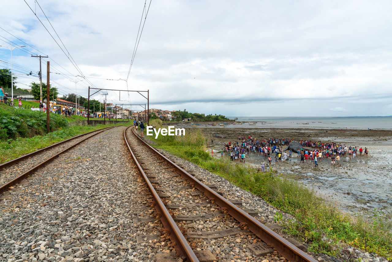 track, railroad track, rail transportation, sky, transportation, cloud, transport, nature, railway, mode of transportation, water, group of people, travel, vehicle, sea, land, day, crowd, vanishing point, large group of people, public transportation, cable, beach, outdoors, architecture, travel destinations, train, electricity, plant, the way forward, diminishing perspective