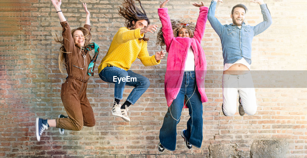 Full length of friends jumping against wall
