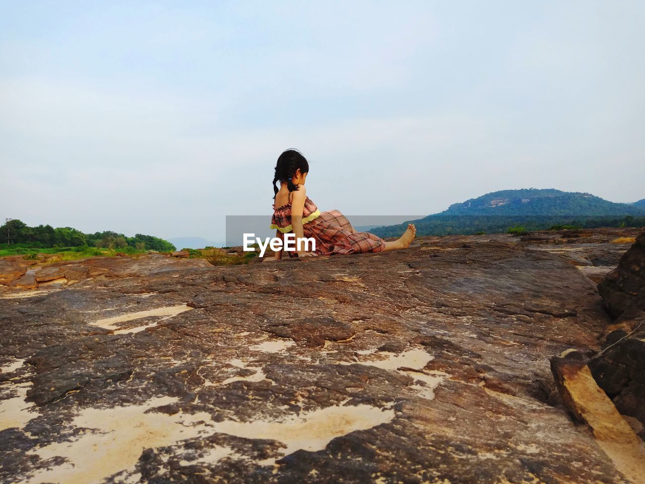 Rear view of girl sitting on rock against sky