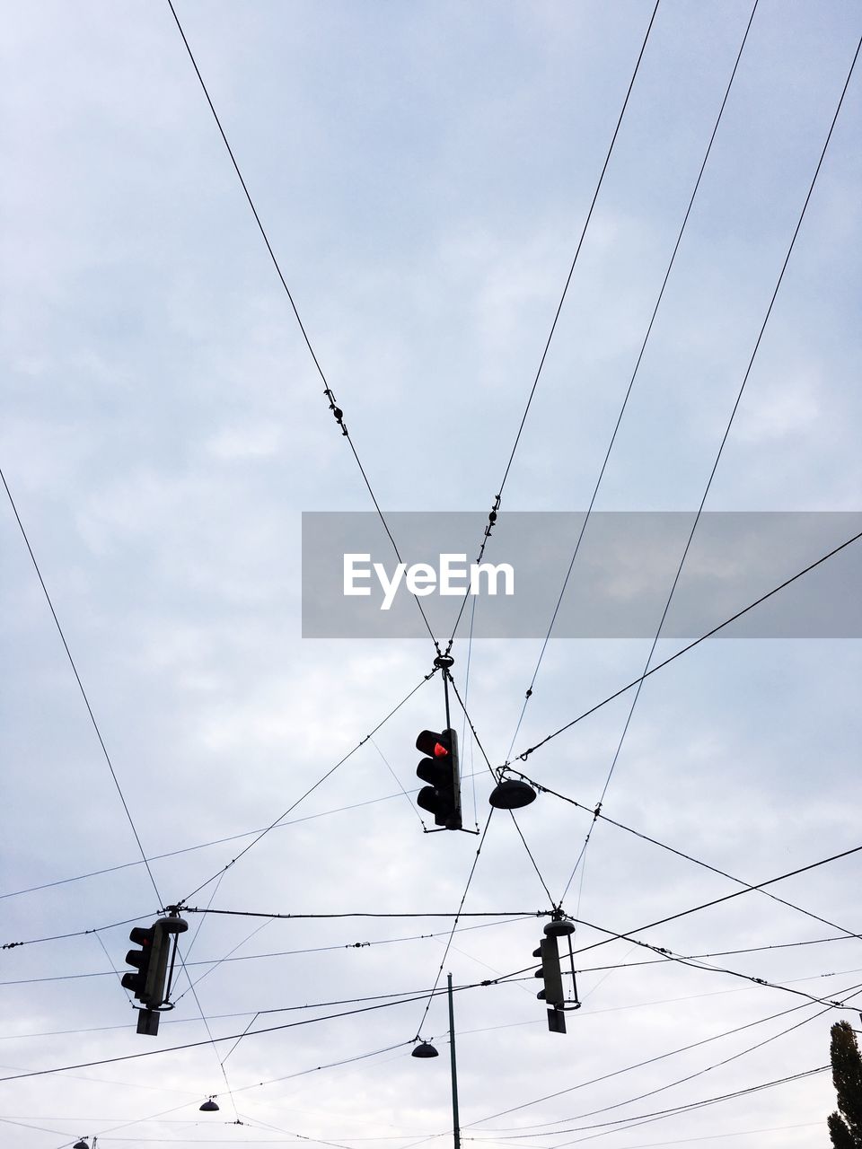 Low angle view of stoplights hanging against cloudy sky