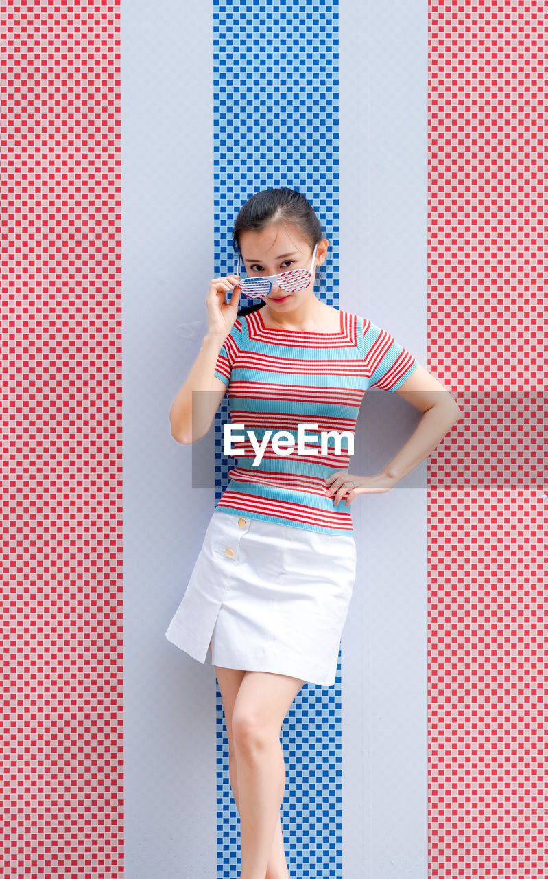 Portrait of woman in sunglasses standing against colorful wall