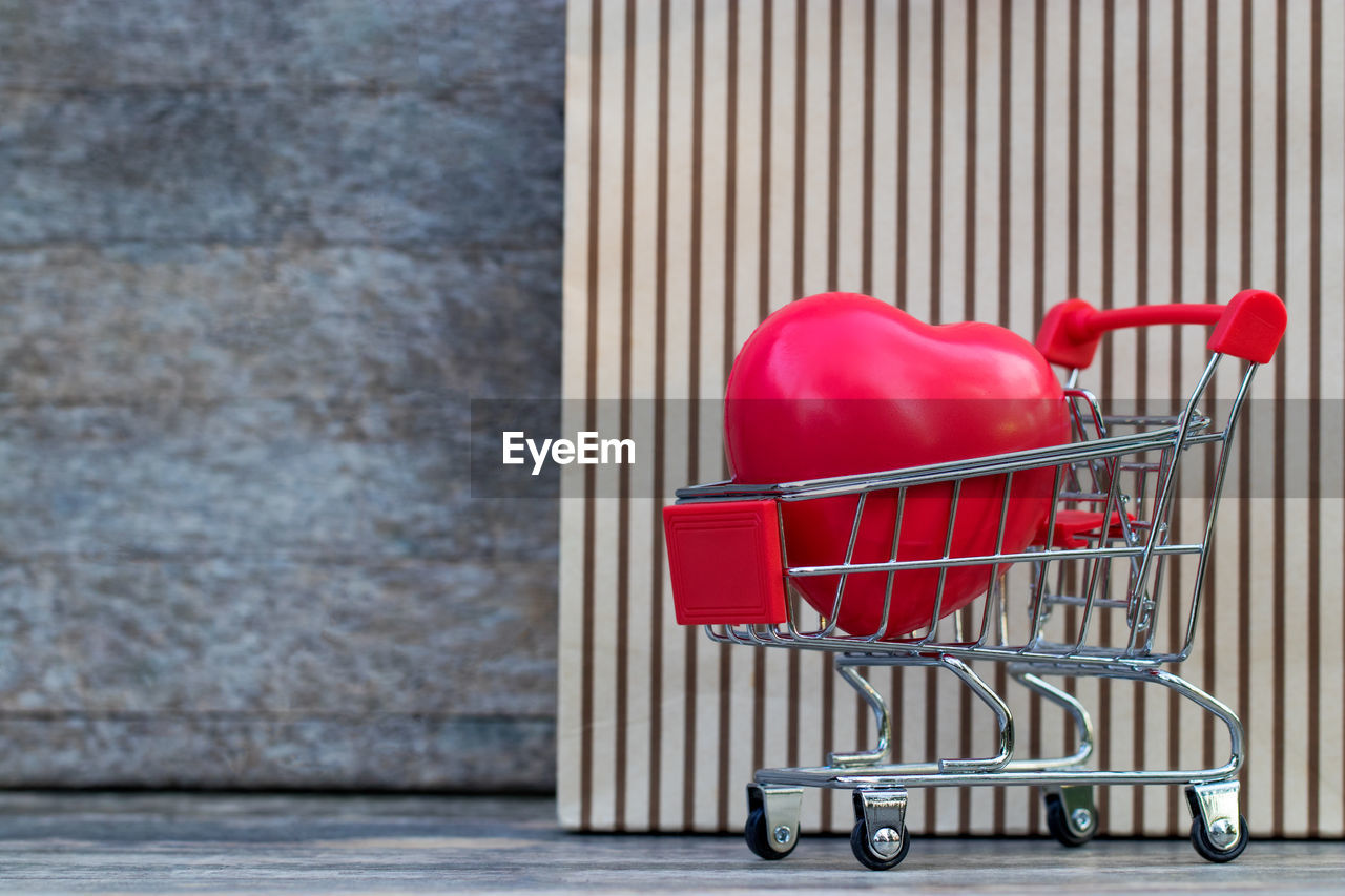 Close-up of red heart shape in shopping cart against wall