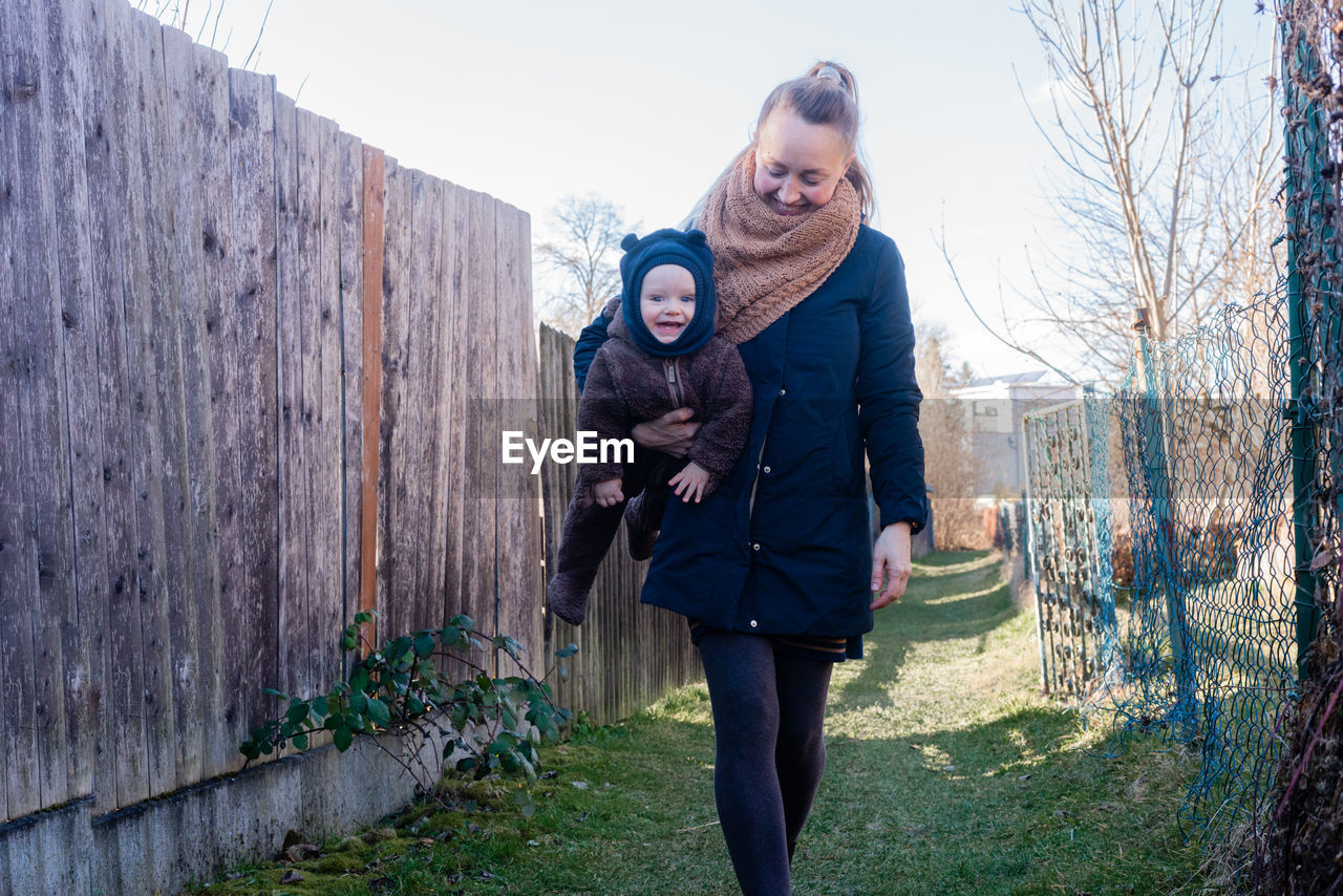 Smiling woman holding happy baby in her hands and against wooden wall. mother and son.