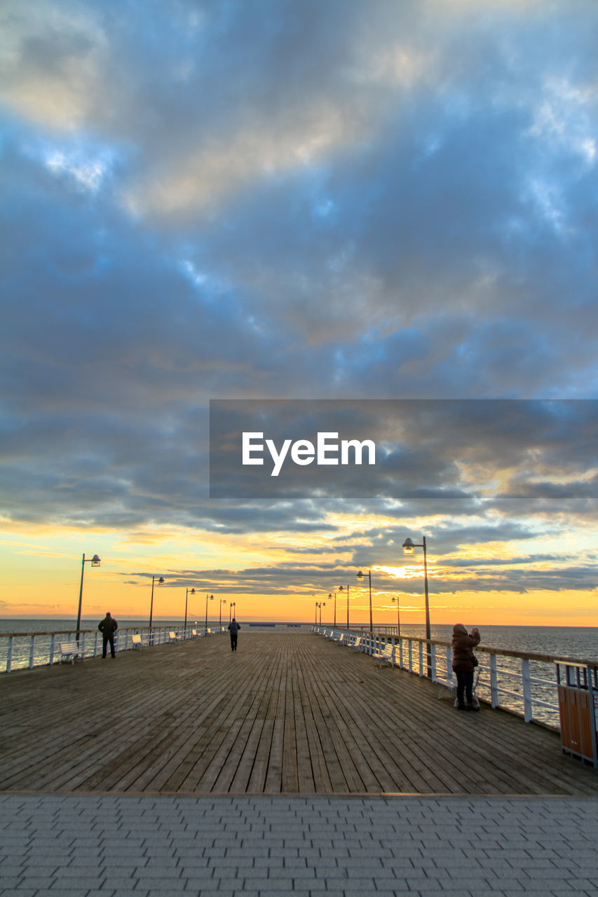 Boardwalk over sea against cloudy sky during sunset