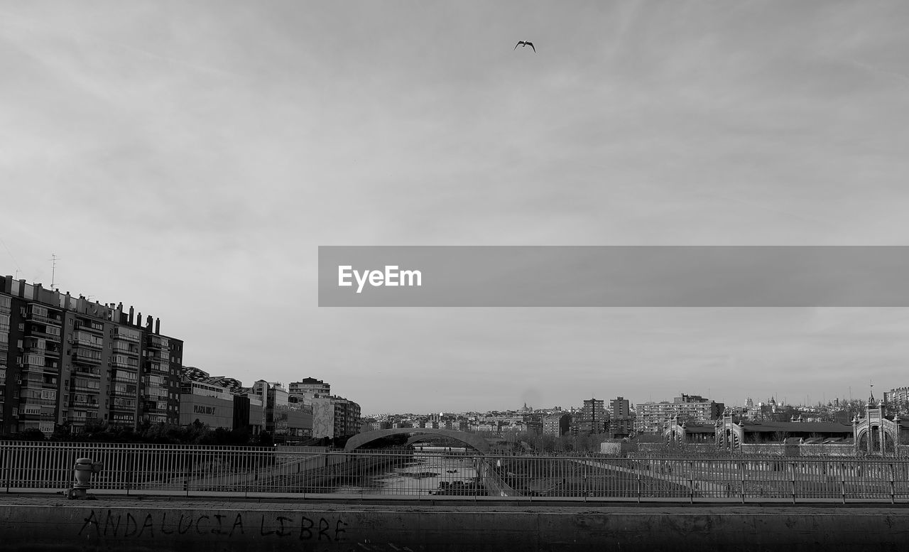 BRIDGE OVER RIVER AMIDST BUILDINGS AGAINST SKY