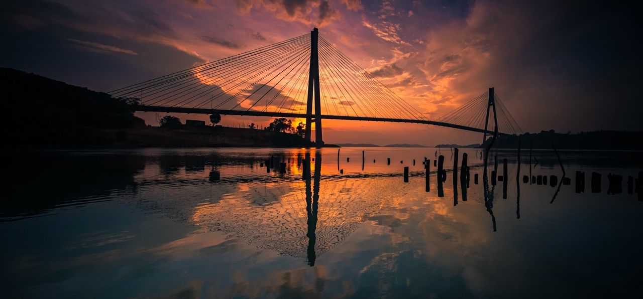 Silhouette barelang bridge over river against cloudy sky during sunset