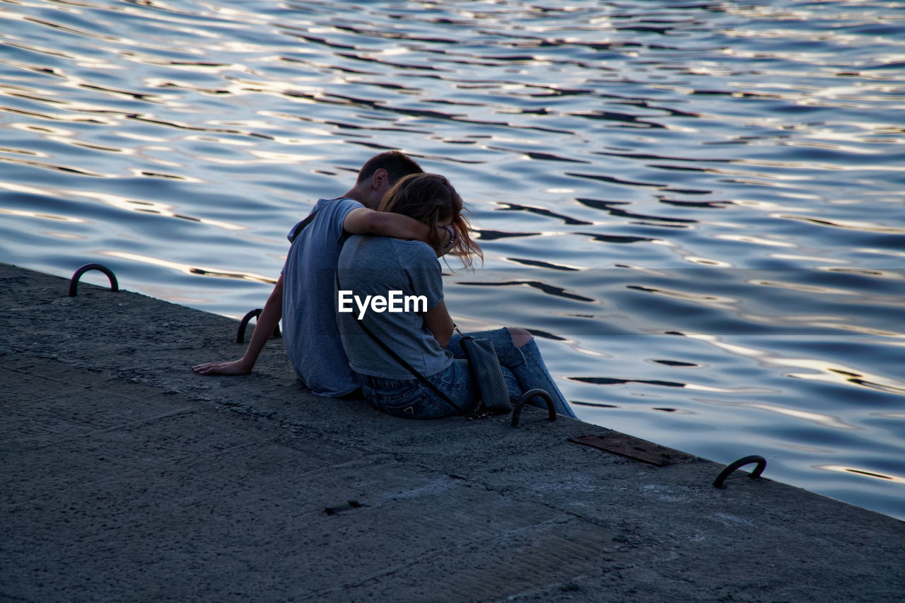 REAR VIEW OF COUPLE SITTING ON BEACH