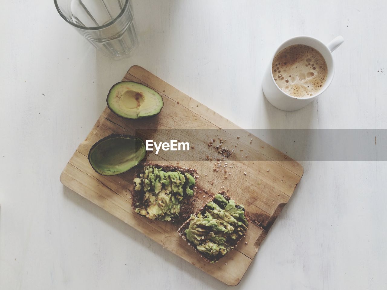 High angle view of avocado and breads by coffee cup on cutting board over table