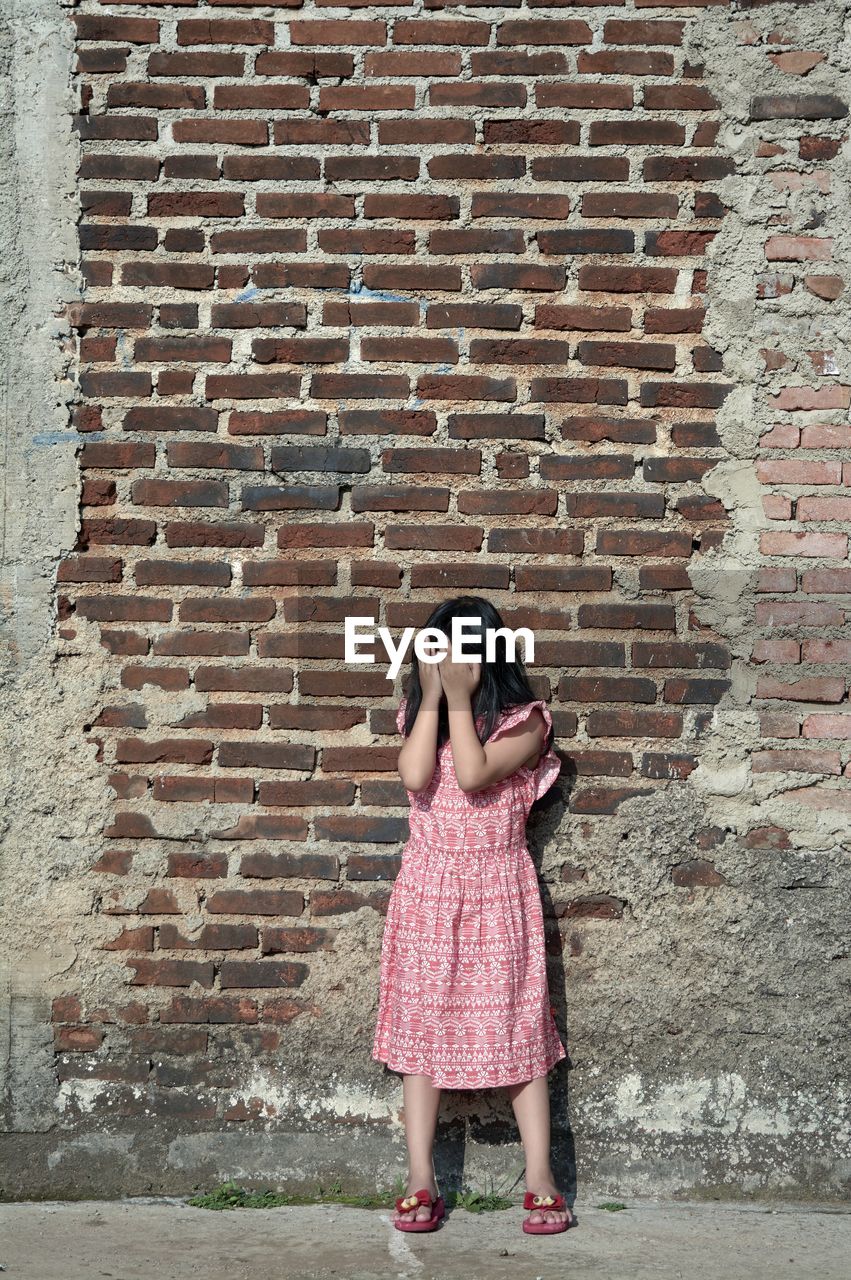 Full length of girl standing against brick wall